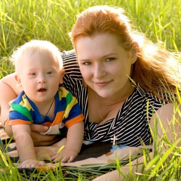 Woman with long red hair holding baby son with down's syndrome, lying together in a field